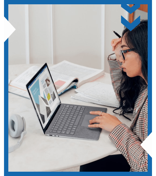 Focused student working on a laptop and taking notes at a study desk with books and headphones